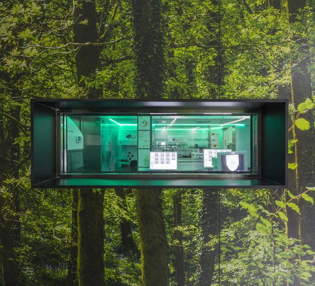 Una farmacia futurista, que recuerda el espíritu innovador del Institut Marqués, se sitúa en un mural de bosque. Encerrada en un cristal con iluminación verde, presenta estanterías con diversos artículos y una pantalla digital. El mostrador de azulejos realza la yuxtaposición armoniosa de naturaleza y tecnología.